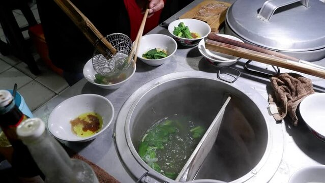 In the process of cooking Chicken Noodles, Indonesian street food, the chef prepares a bowl that has been added secret oil and mustard greens, then pours the cooked noodles into the bowl