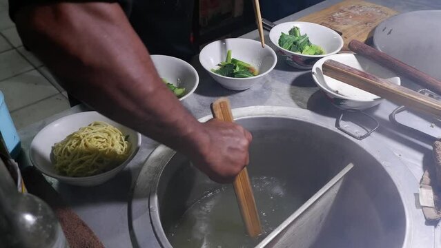 In the process of cooking Chicken Noodles, Indonesian street food, the chef prepares a bowl that has been added secret oil and mustard greens, then pours the cooked noodles into the bowl