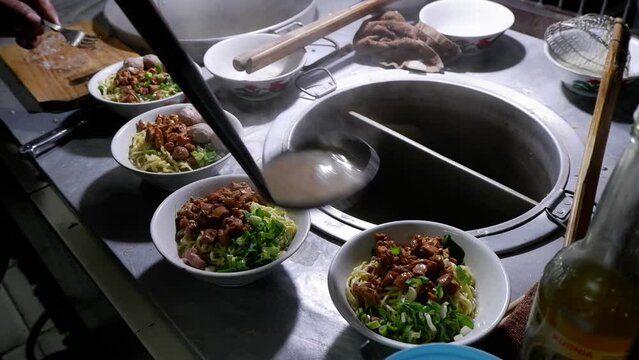 In the process of cooking Chicken Noodles, Indonesian street food, the chef prepares a bowl that has been added secret oil and mustard greens, then pours the cooked noodles into the bowl