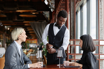 Portrait of server showing label on red wine bottle to couple enjoying dinner in luxury restaurant