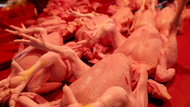 A seller of chicken meat in a traditional market at night who is serving customers, cutting and weighing the meat purchased.