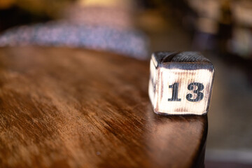 The number 13 on the wooden cube is burned with large symbols. The cube stands on the right in the frame on an empty smooth wooden table of dark color. The upper face of cube has a charred appearance.