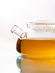 Glass teapot  tea on light background with reflection