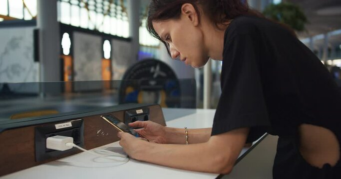 Young woman traveler charging smartphone and working at airport while waiting boarding