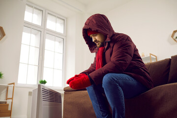 Man sitting by the heater when it's freezing cold in the house in winter. Man in winter clothes...