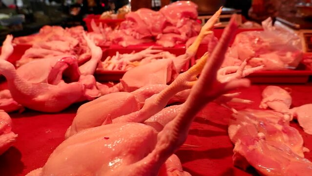 A seller of chicken meat in a traditional market at night who is serving customers, cutting and weighing the meat purchased.