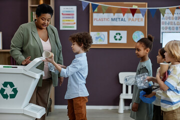 Side view portrait of Black woman teaching little kids about recycling and waste sorting in...