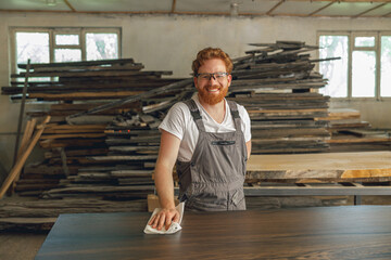 Portrait of smiling carpenter in eyeglasses standing on the background on carpentry workshop