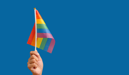 Rainbow flag showing in hand against a blue background.