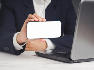Businessman holding a white blank screen smartphone horizontally while sitting at the table.
