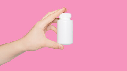 Hand with empty white pill bottle isolated on pink background. Copy space. Bottle with pills....