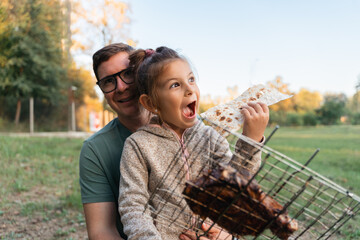 Child girl with father portrait outdoors with grill bbq net with beef steak meat. Happy family...