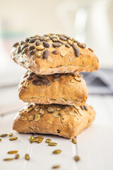 Whole grain bun with pumpkin seeds on white table.