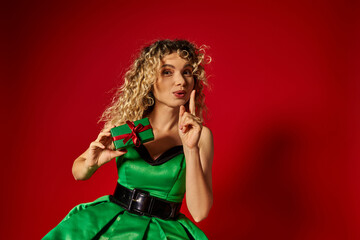 attractive new year elf in green dress showing silence gesture mysteriously with gift in hands