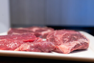A large and delicious grilled beef steak is a great way to taste meat and freshly prepared homemade dishes. The photo shows three large pieces of raw meat in a white plate,the frame is shot from below