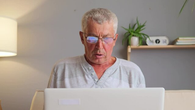 Sad despair senior man using his laptop in home interior having problems with software looking at display with scared expression making mistake on web pages.