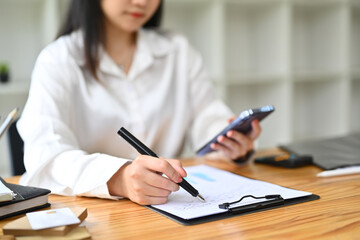 Female secretary holding mobile phone and writing appointments, schedule and business contacts at desk