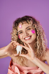 cheerful lovely woman with curly hair and face stickers holding baby tooth and smiling at camera