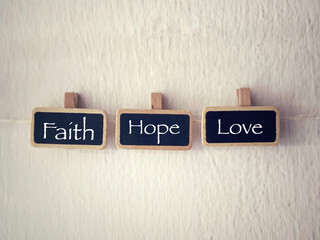 Motivational and inspirational wording. Christianity concept. FAITH, HOPE and LOVE words written on wooden tags. With blurred styled background.
