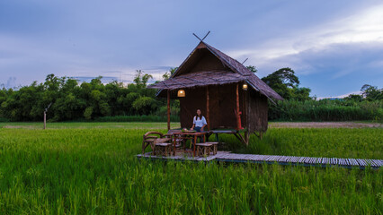 Fototapeta na wymiar Asian woman on vacation at a small homestay at the farm with a green rice paddy field in Central Thailand