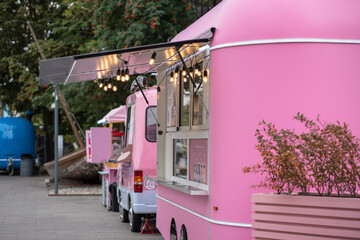 Pink ice cream vans on empty street in city, mobile fair trade with food trucks. Cafe in transport, cafeteria business. Modern urban infrastructure in vintage style, junk unhealthy food concept.