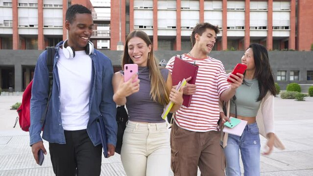 A group of students walks from outside. Students classmates walk down the street talking and laughing together while looking at social networks on the mobile phone