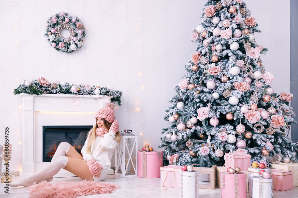 Wall mural Smiling young woman in knitted clothes sits by the fireplace. be