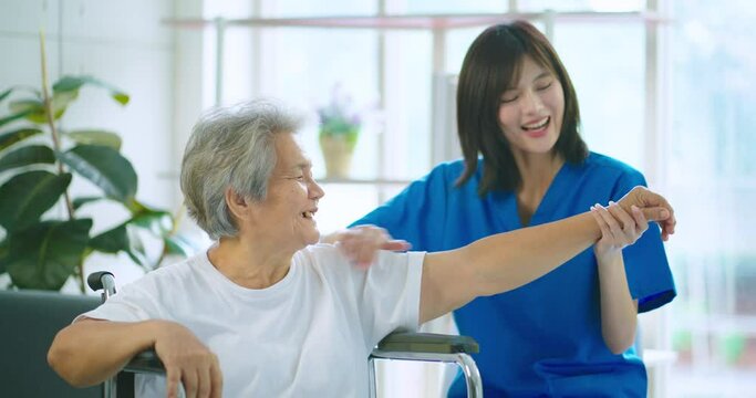 Beautiful asian nurse taking care of senior woman sitting oh wheelchair to exercise at hospital. She feeling happy when take care senior woman.