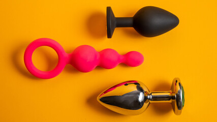 A set of three alternative sex devices of various shapes and sizes on an orange background....