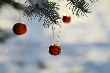 Red Christmas bell hangs on a snow-covered branch of a Christmas tree against a festive background of white snow. New Year, greeting and holiday card, banner.