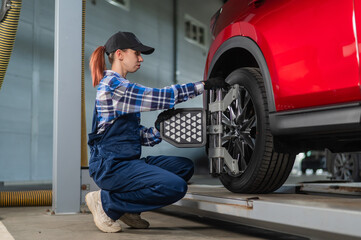 A female auto mechanic makes a camber. Woman working in a car service. - obrazy, fototapety, plakaty