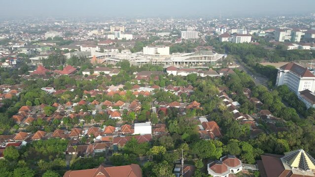 Aerial view of Jogja City with dense buildings development, crowded vehicles traffic in morning sunlight with smog or fog. Population density is displacing agricultural land and forests. Air Pollution