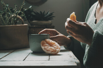 Close up of woman eating orange fruit and drinking herbal tea or coffee at home. healthy food and...