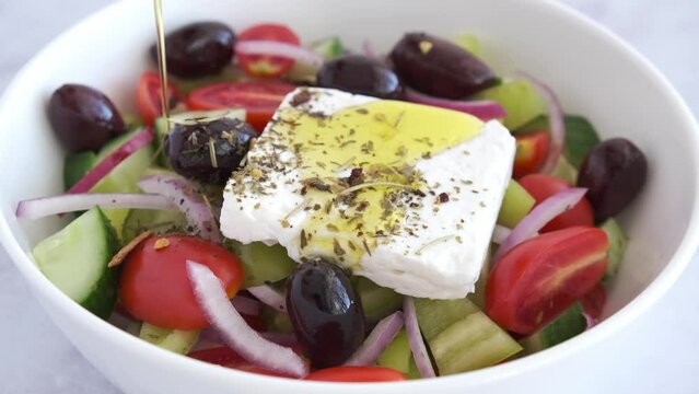 Bowl of traditional Greek salad with tomatoes, cucumbers, red onions, kalamata olives, feta sheep cheese and olive oil.