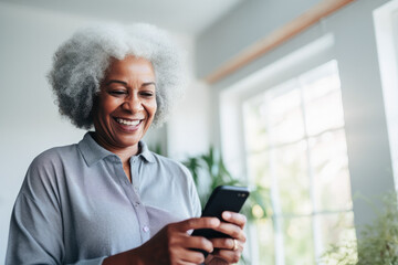 Portrait of a relaxed senior woman laughing while using her smartphone at home. Modern lifestyle of the elderly people.  - obrazy, fototapety, plakaty