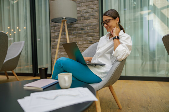 Professional female analist in eyeglasses working on laptop while sitting in modern coworking 
