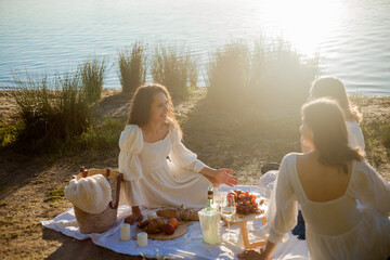 Young beautiful women of 25 years old on an autumn picnic near the lake. Glass of white wine, pastries. Happy models chatting merrily. Sunset.