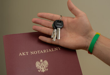 Klucz do nowego mieszkania trzymany na tle aktu notarialnego  - obrazy, fototapety, plakaty