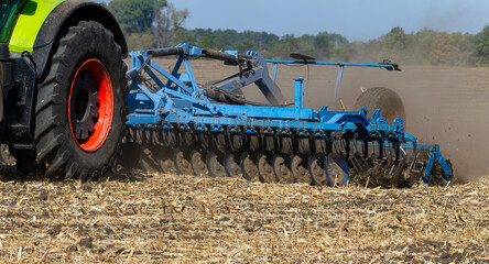 The tractor works in the field with a plow with a disc harrow. Seasonal tillage for subsequent sowing of grain. Photo series