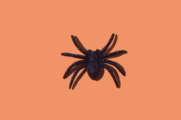 Shiny plastic spider as a decoration for Halloween, on an orange background. Concept of terror, phobia, fear, celebration, arachnophobia, day of the dead, disgust, repellent and toy.