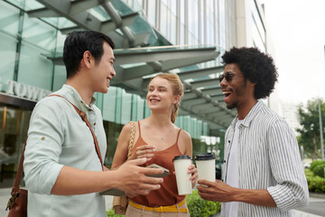 Cheerful coworkers standing out office building, drinking coffee and discussing news