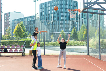 Fototapeta na wymiar summer holidays, sport and people concept - happy family with ball playing on basketball playground