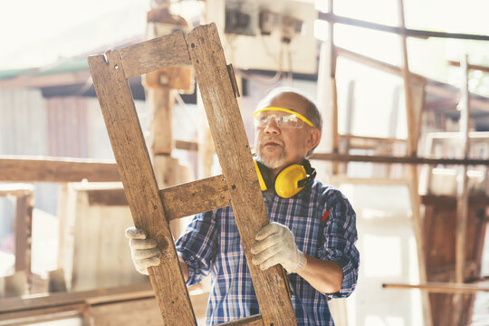 Senior Asian male carpenter working and inspecting quality of wood frame at furniture workshop. Asian male joiner working at woodwork workshop