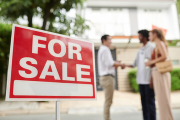 For sale sign and couple greeting real estate agent in background