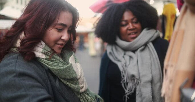 Happy multiracial female friends doing shopping at christmas street market during winter time outdoor