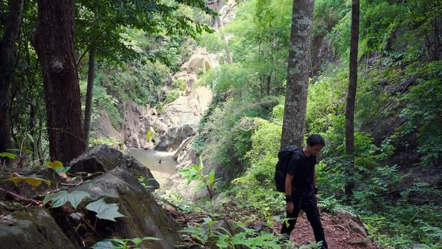 people activity concept with asian man hiking and see to waterfall in tropical forest 