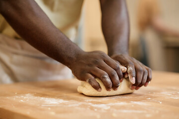 Close up of young Black man kneading dough while making fresh bread in artisan bakery, copy space