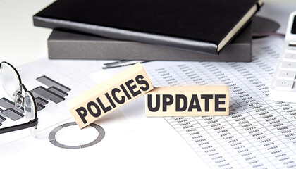 POLICIES UPDATE - text on a wooden block with chart and notebook