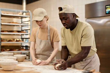 Close up of two young people preparing fresh dough for bread baking in bakery kitchen, copy space