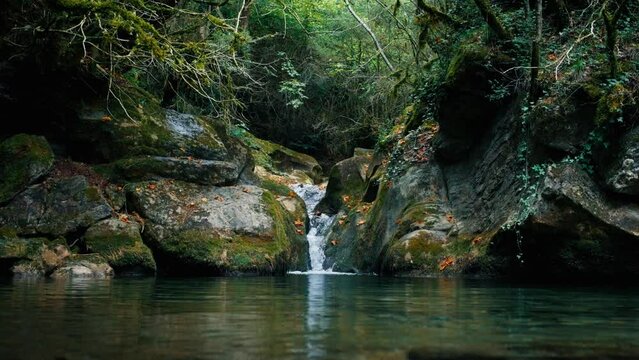Cinematic shot of flowing waterfall on mountain river into pond in green forest